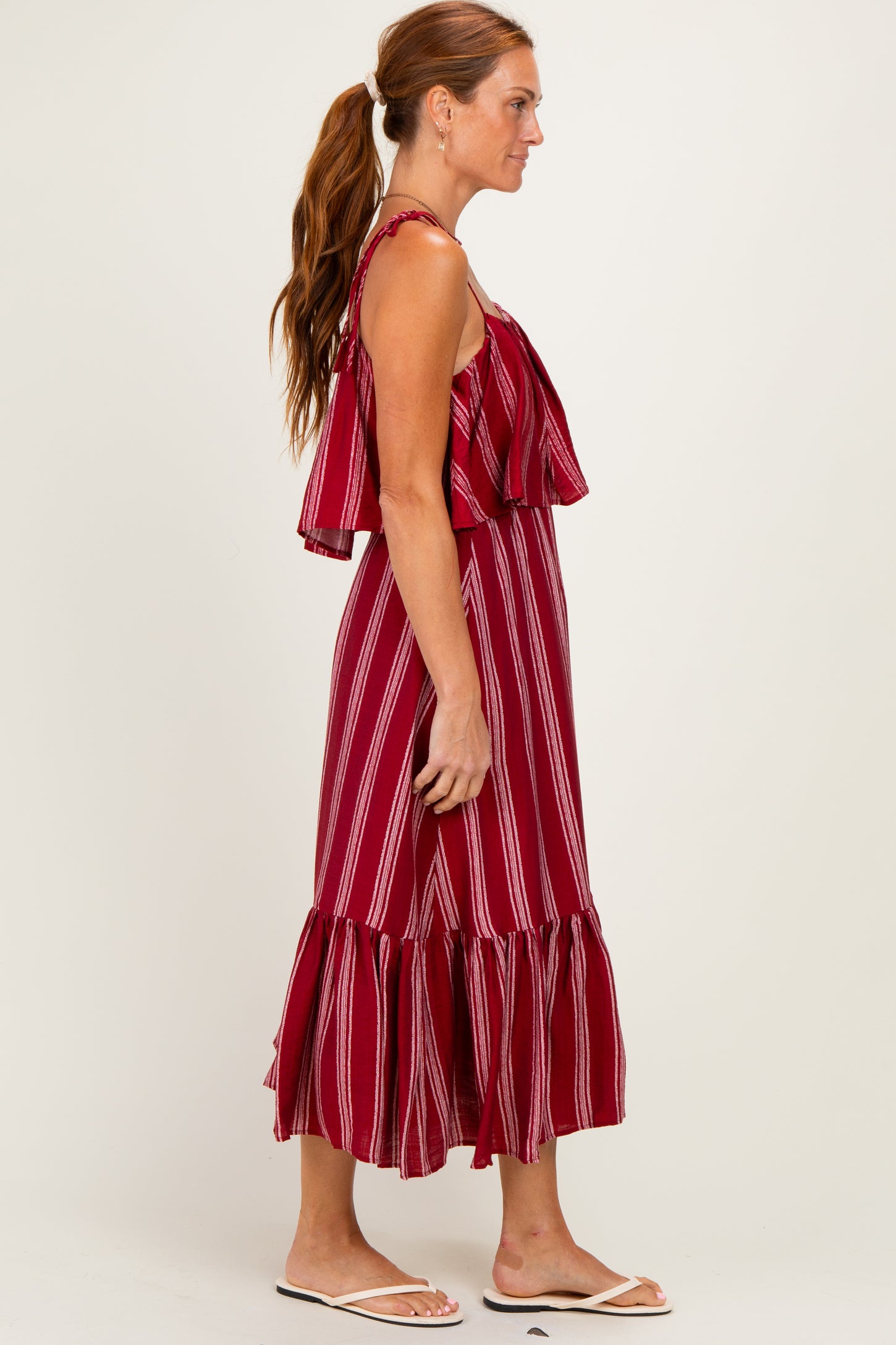 woman wearing a burgundy striped maxi dress with ruffled straps and a tiered hemline, standing sideways
