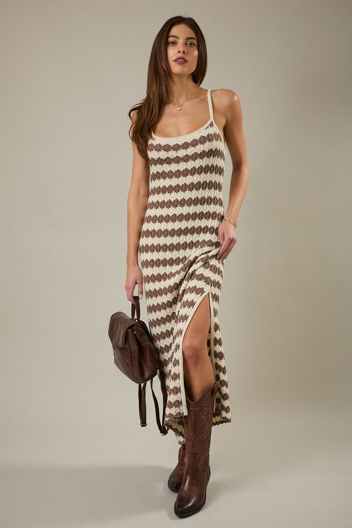 woman wearing a beige and brown patterned maxi dress with a side slit and brown cowboy boots, posing with a brown handbag