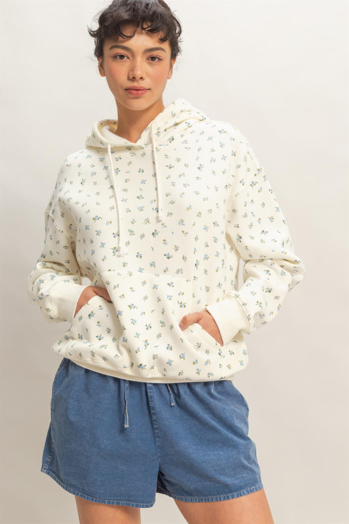 woman wearing a cream floral print hoodie with a front pocket and blue denim shorts
