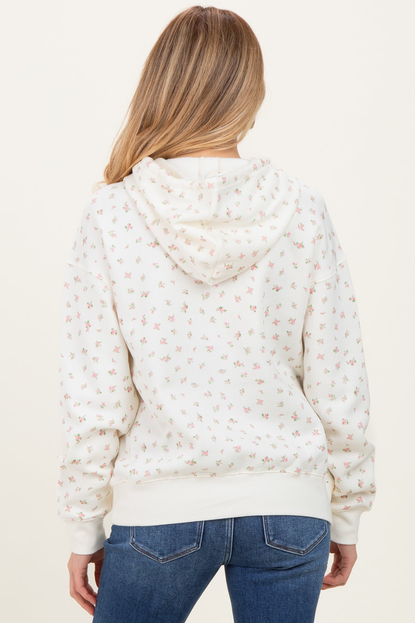 woman wearing a cream floral maternity hoodie with a hood, seen from the back, paired with blue jeans