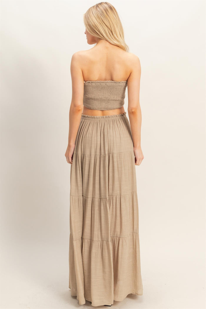 woman wearing a beige two-piece strapless top and long tiered maxi skirt, shown from the back