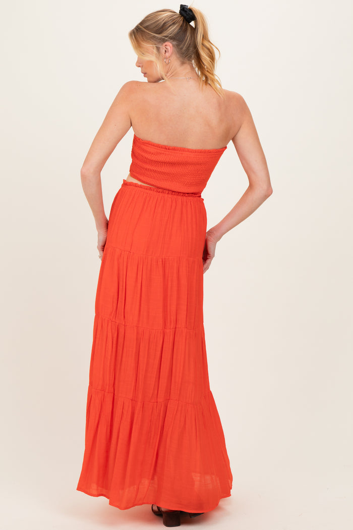 woman wearing an orange strapless maternity maxi dress with tiered skirt and smocked bodice, showing her back