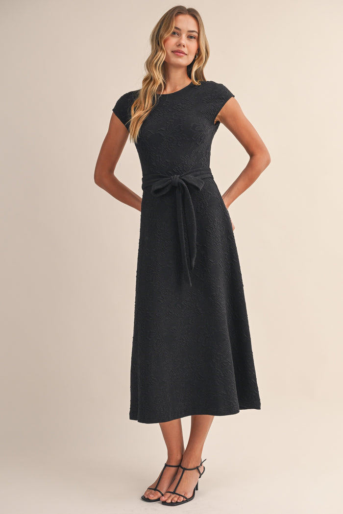 woman wearing a black cap sleeve belted midi dress with textured floral design
