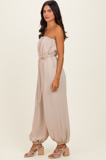 woman wearing a light beige off-the-shoulder jumpsuit with a tie waist and balloon-style pant legs