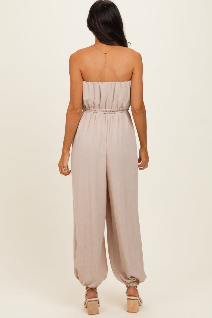 woman wearing a strapless beige jumpsuit with a gathered waistband and relaxed fit, showing the back view