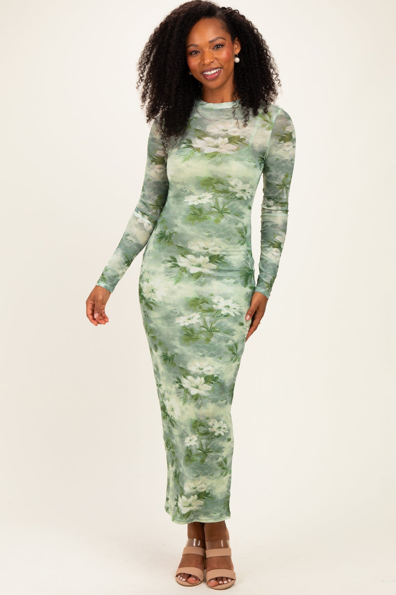 woman wearing a long sleeve green floral maxi dress with a fitted silhouette and a sheer overlay