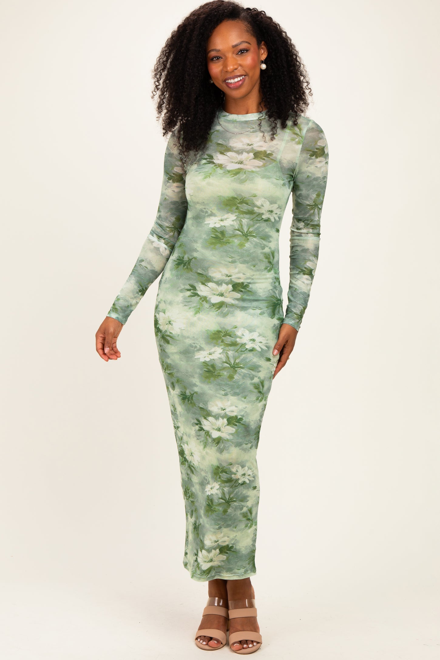 woman wearing a long sleeve green floral maxi dress with a fitted silhouette and a sheer overlay