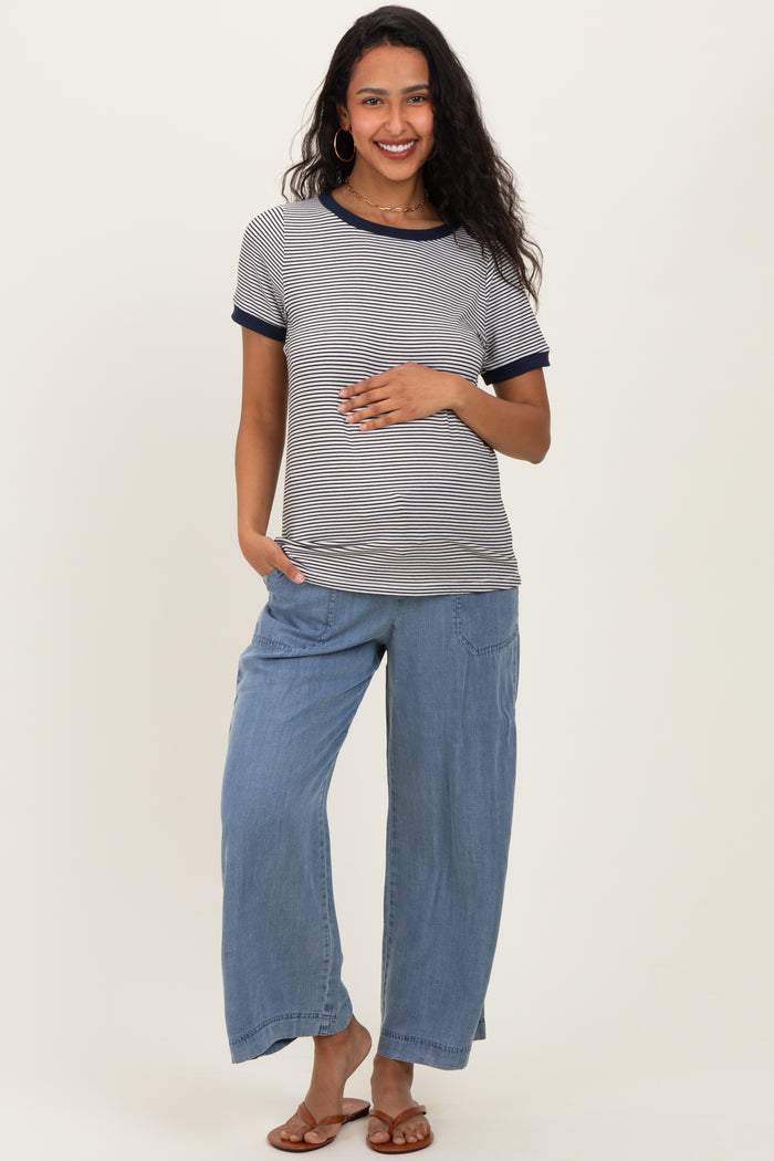woman wearing a striped maternity top with navy trim and loose blue maternity pants, holding her baby bump