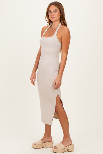 woman wearing a light beige ribbed midi dress with a side slit and halter neckline, styled with wedge sandals
