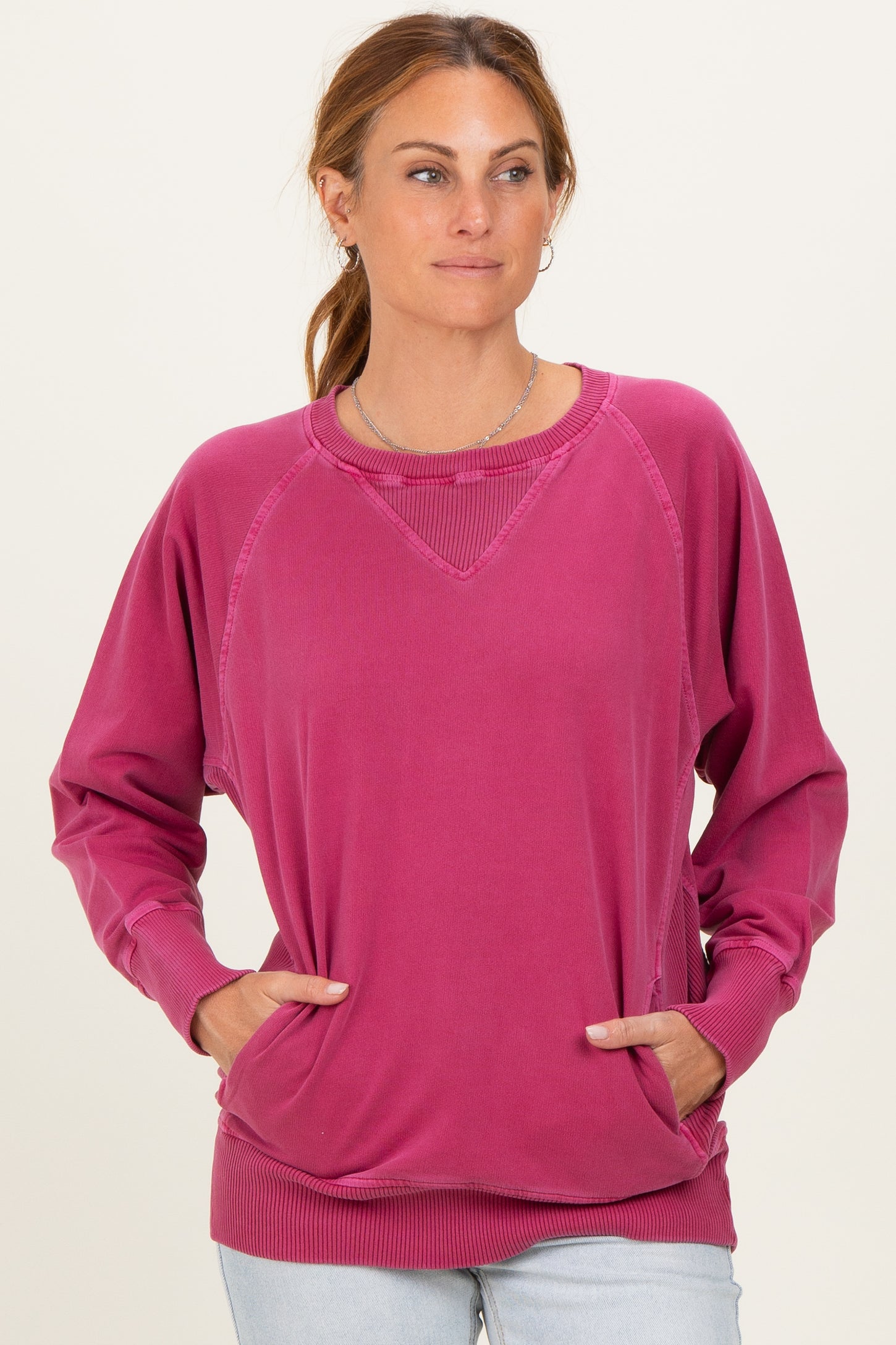 woman wearing a pink oversized sweater with raglan sleeves and side pockets, styled casually with light wash jeans