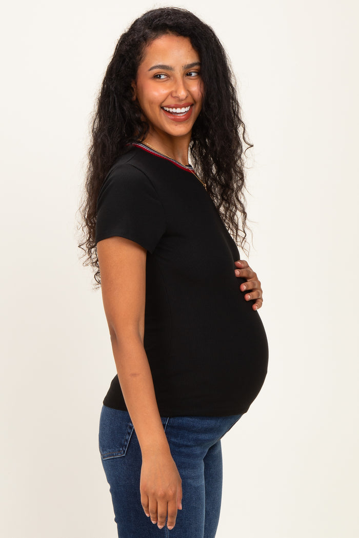 woman wearing a black maternity top with a colorful neckline and showing off her baby bump while smiling