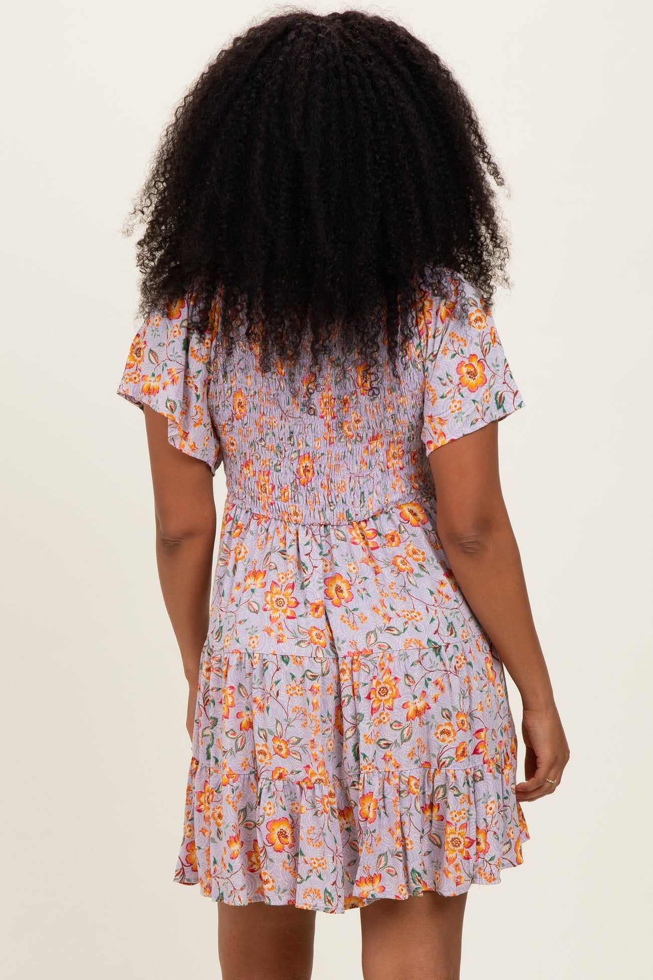 woman wearing a floral print short dress with a smocked back and ruffled hem standing with her back to the camera