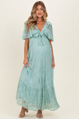 woman wearing a light blue lace maternity dress with a tie front and flutter sleeves, showing her baby bump