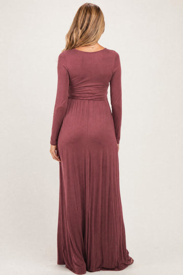 woman wearing a burgundy long sleeve maternity maxi dress with a fitted waist and flowing skirt, view from the back