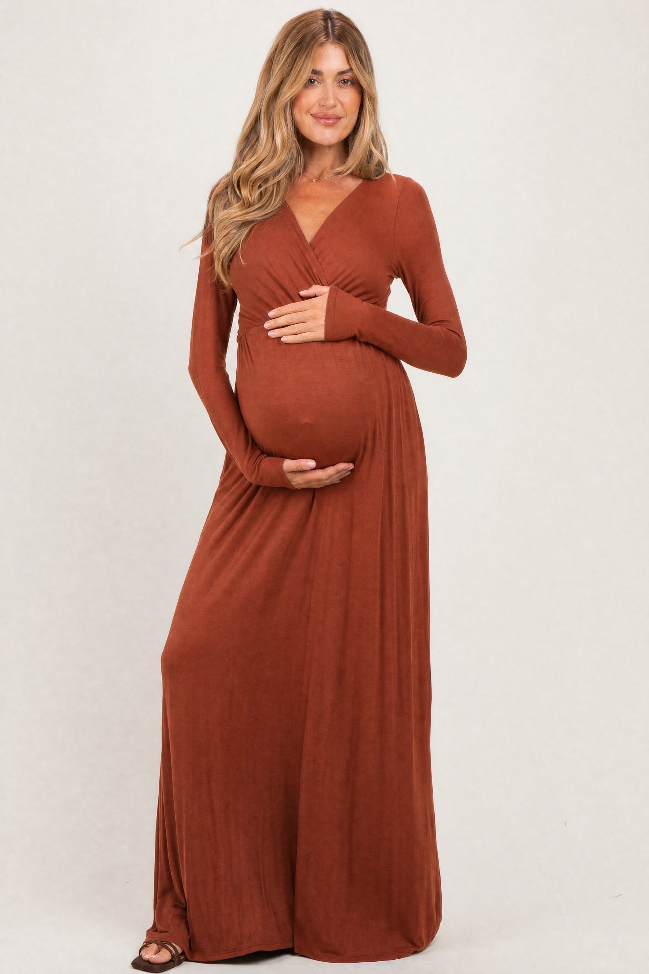 woman wearing a rust long sleeve maternity dress with a fitted silhouette and holding her baby bump