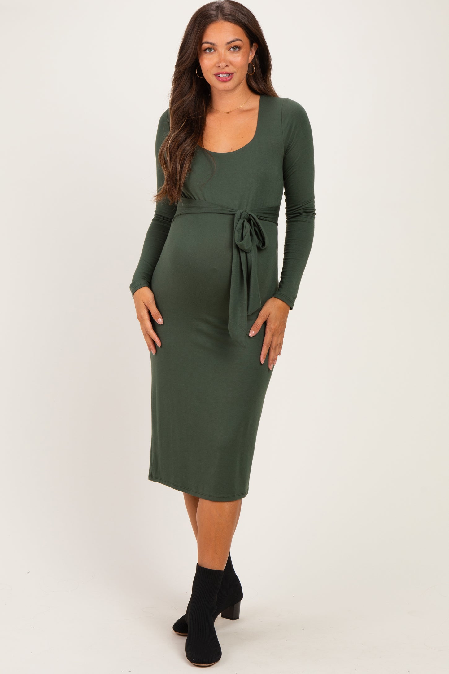 woman wearing a dark green long sleeve maternity dress with a tie at the waist and a visible baby bump