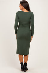 woman wearing a dark green long sleeve maternity dress, with a fitted silhouette and knee-length hem