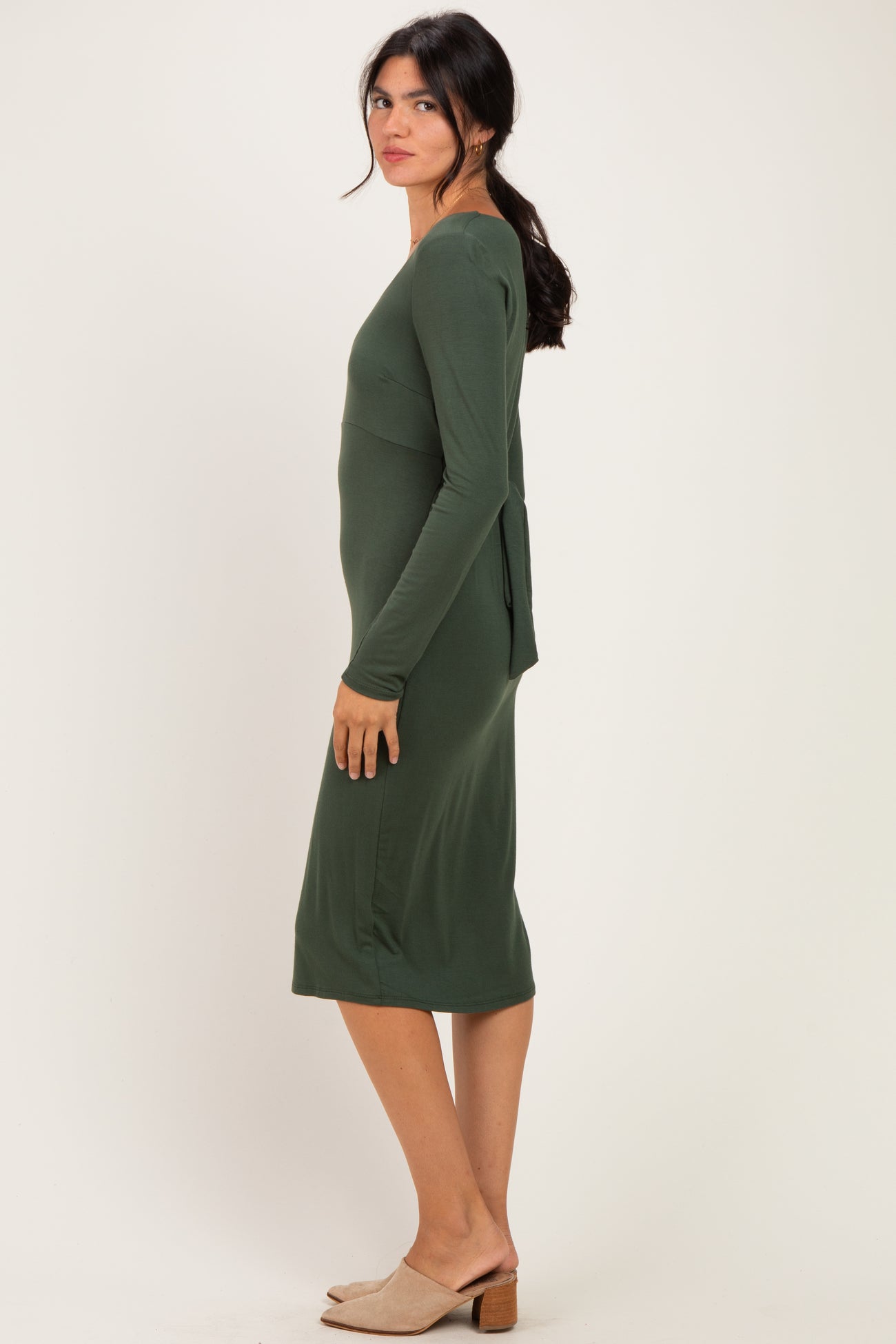 woman wearing a dark green long sleeve fitted dress with a back tie detail and a knee-length hemline