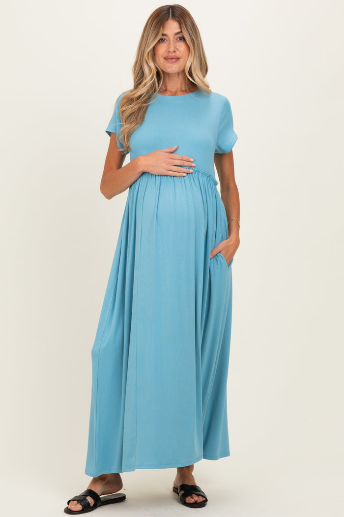 woman wearing a light blue full-length maternity dress with short sleeves and side pockets, holding her baby bump