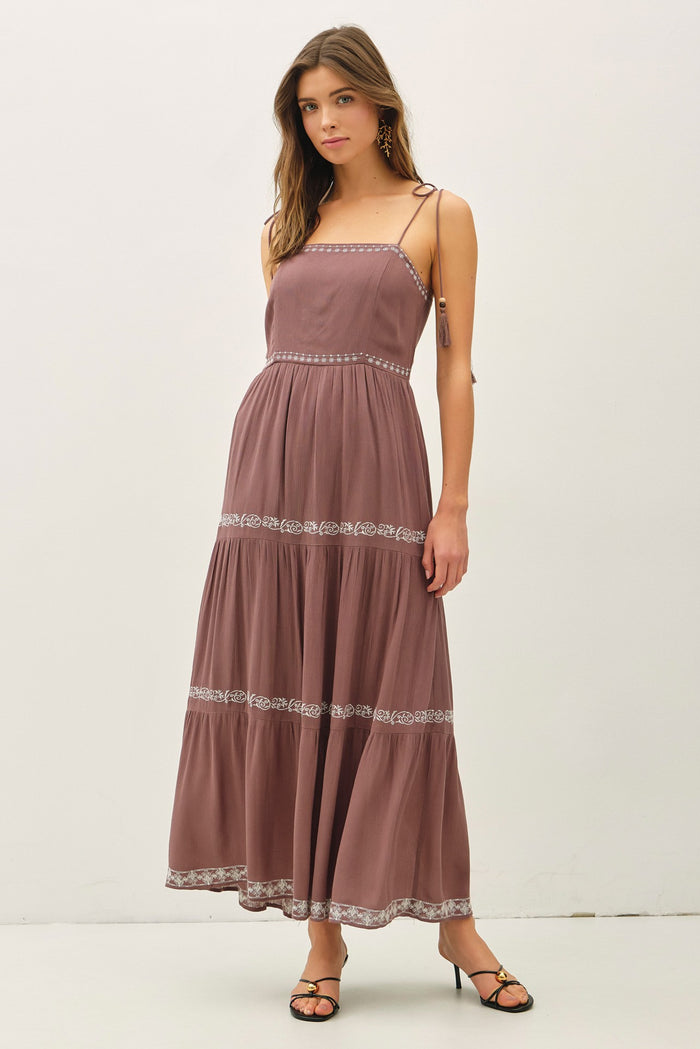 woman wearing a mauve maxi dress with spaghetti straps and floral embroidery, standing and modeling the dress