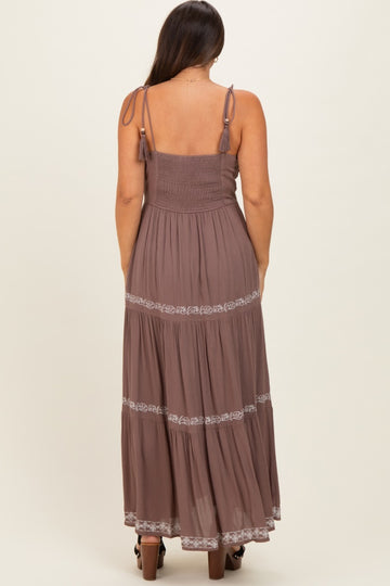 woman wearing a brown maternity maxi dress with adjustable straps and embroidered details on the tiers