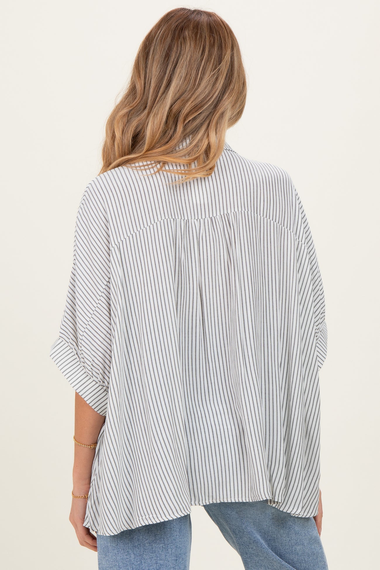 woman wearing a striped maternity top with a flowy back and loose sleeves, styled with light blue jeans