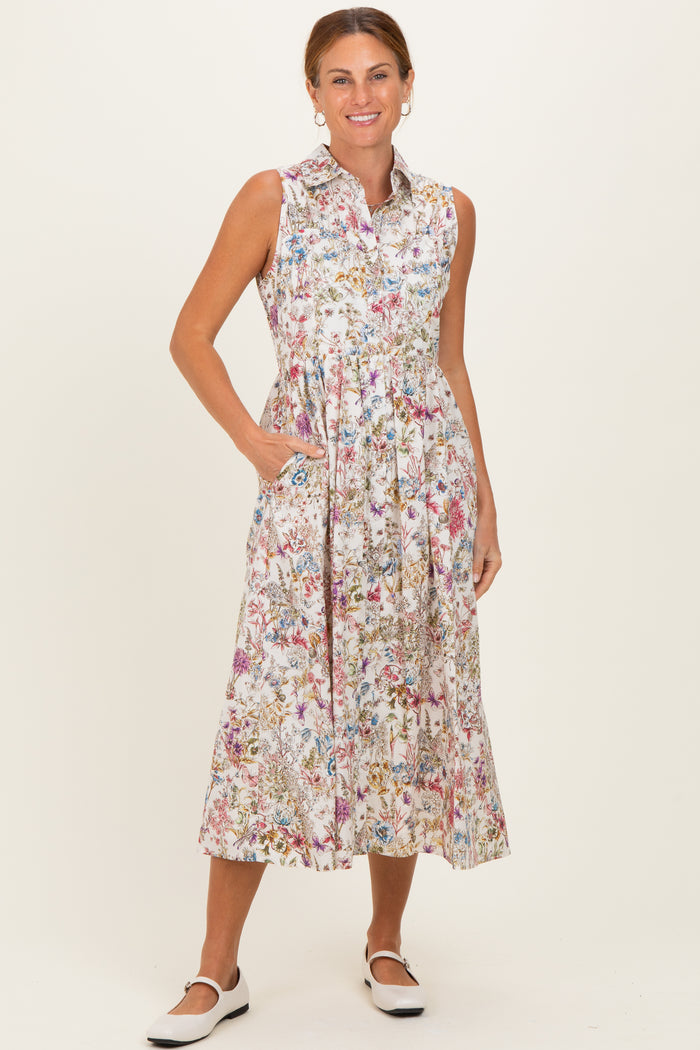 woman wearing a sleeveless floral midi dress with a collar and pockets, standing with a smile