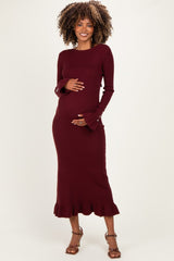 woman wearing a burgundy long sleeve maternity dress with flared cuffs and a ruffled hem, holding her baby bump