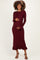 woman wearing a burgundy long sleeve maternity dress with flared cuffs and a ruffled hem, holding her baby bump