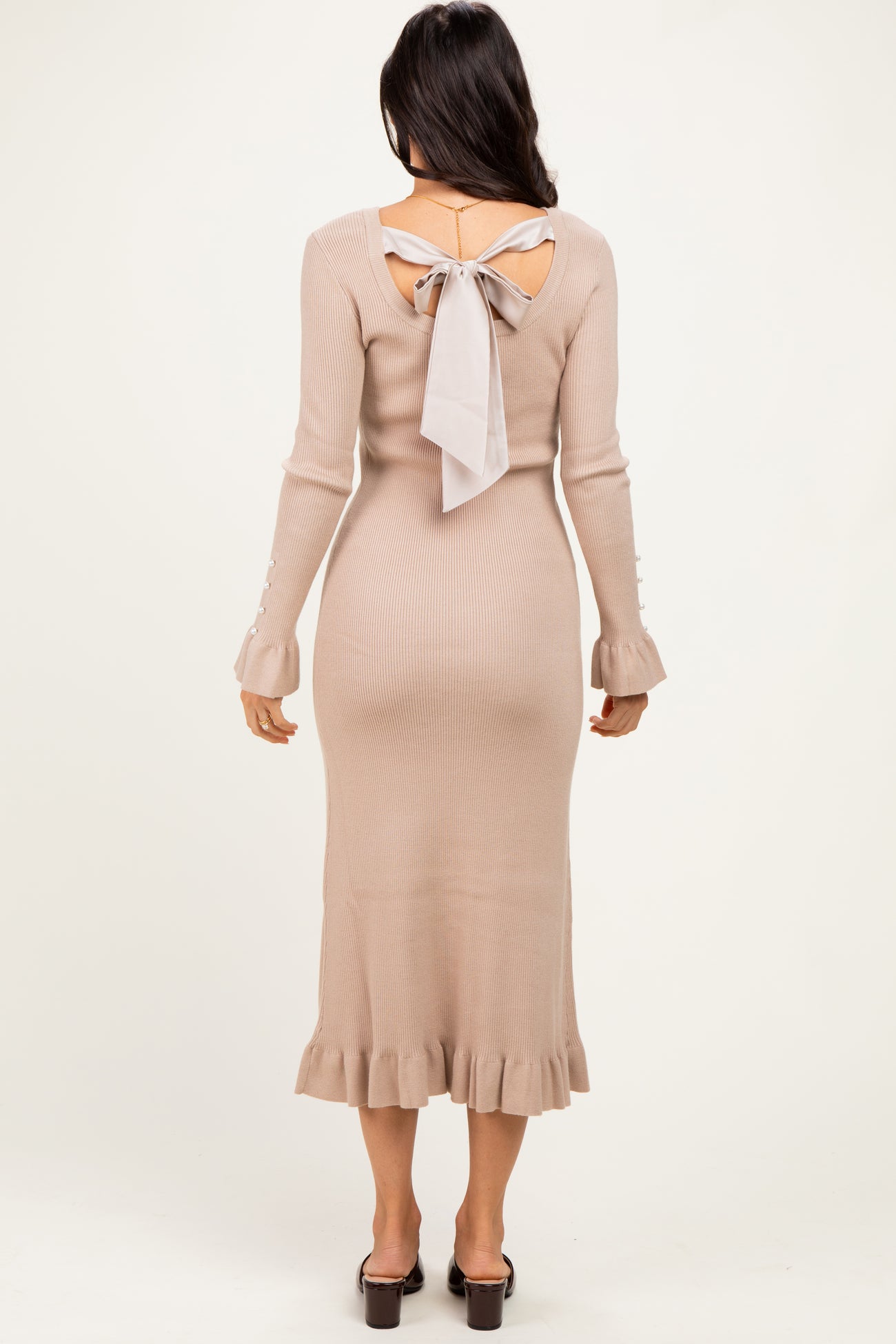 woman wearing a beige ribbed midi dress with a tie-back and ruffle hem details, viewed from the back