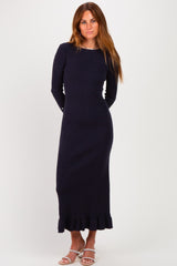 woman wearing a navy long sleeve ribbed dress with a ruffled hem and standing against a plain background
