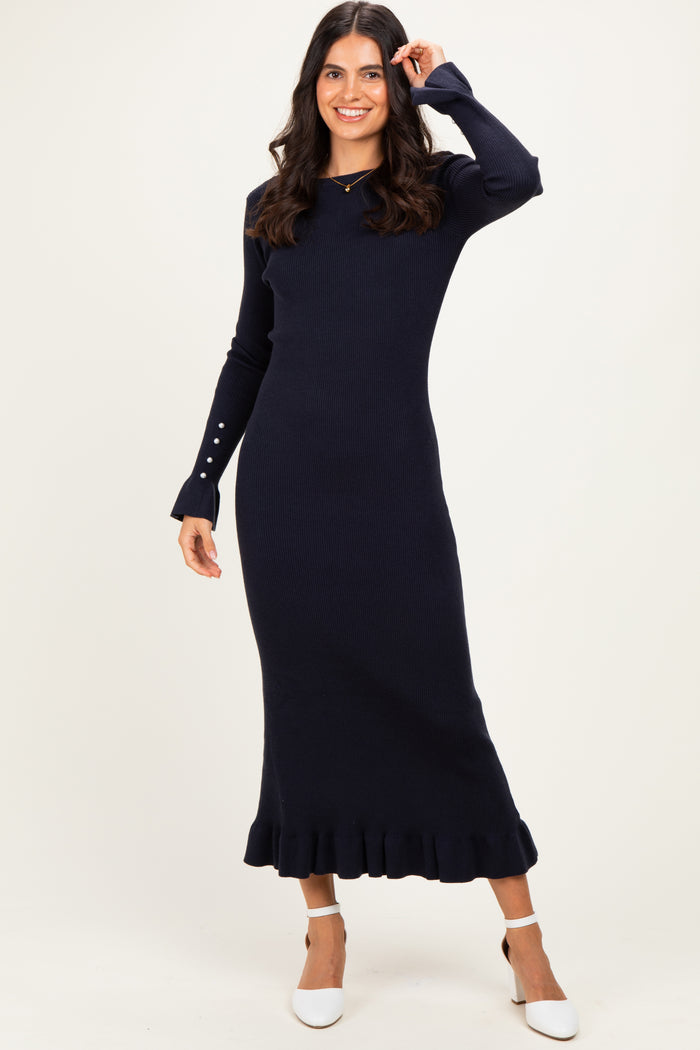 woman wearing a navy blue ribbed midi dress with long sleeves and ruffle hem, standing and smiling