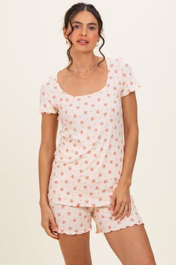 woman wearing a short sleeve floral patterned pajama set in soft peach tones with scalloped edges and shorts