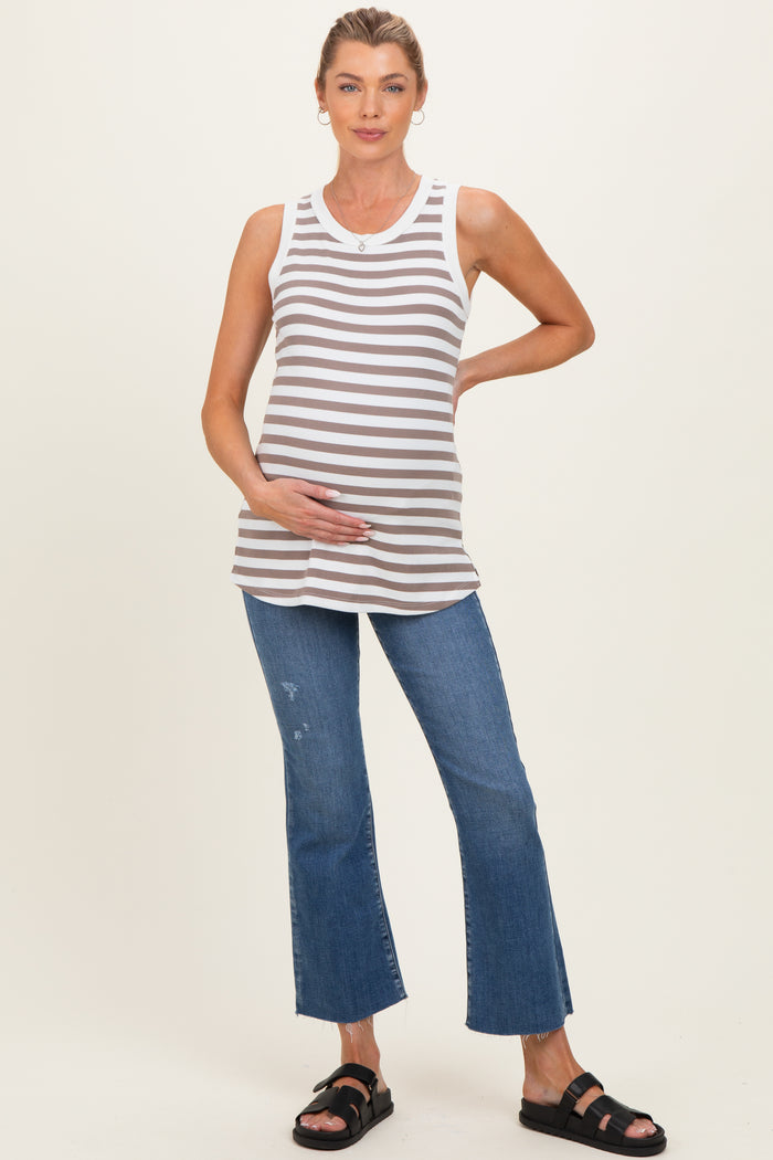 woman wearing a gray and white striped maternity tank top and distressed blue flared jeans, gently holding her baby bump