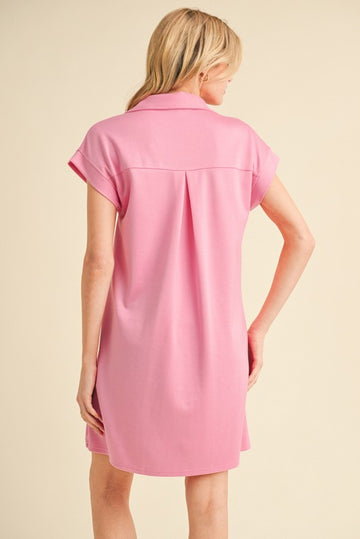 woman wearing a light pink short sleeve shirt dress with a collar and back pleat detail