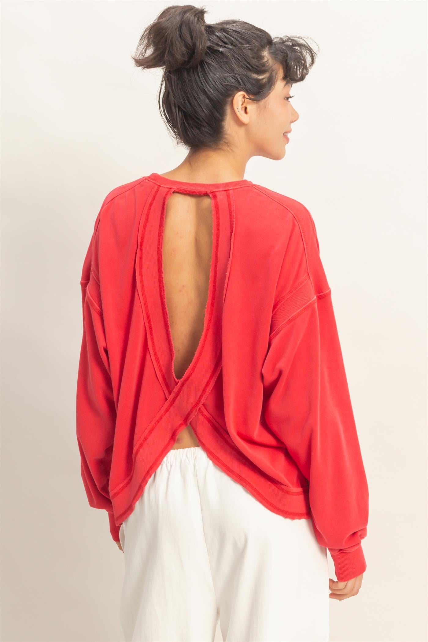 woman wearing a red oversized sweatshirt with an open back and long sleeves, styled casually with white pants