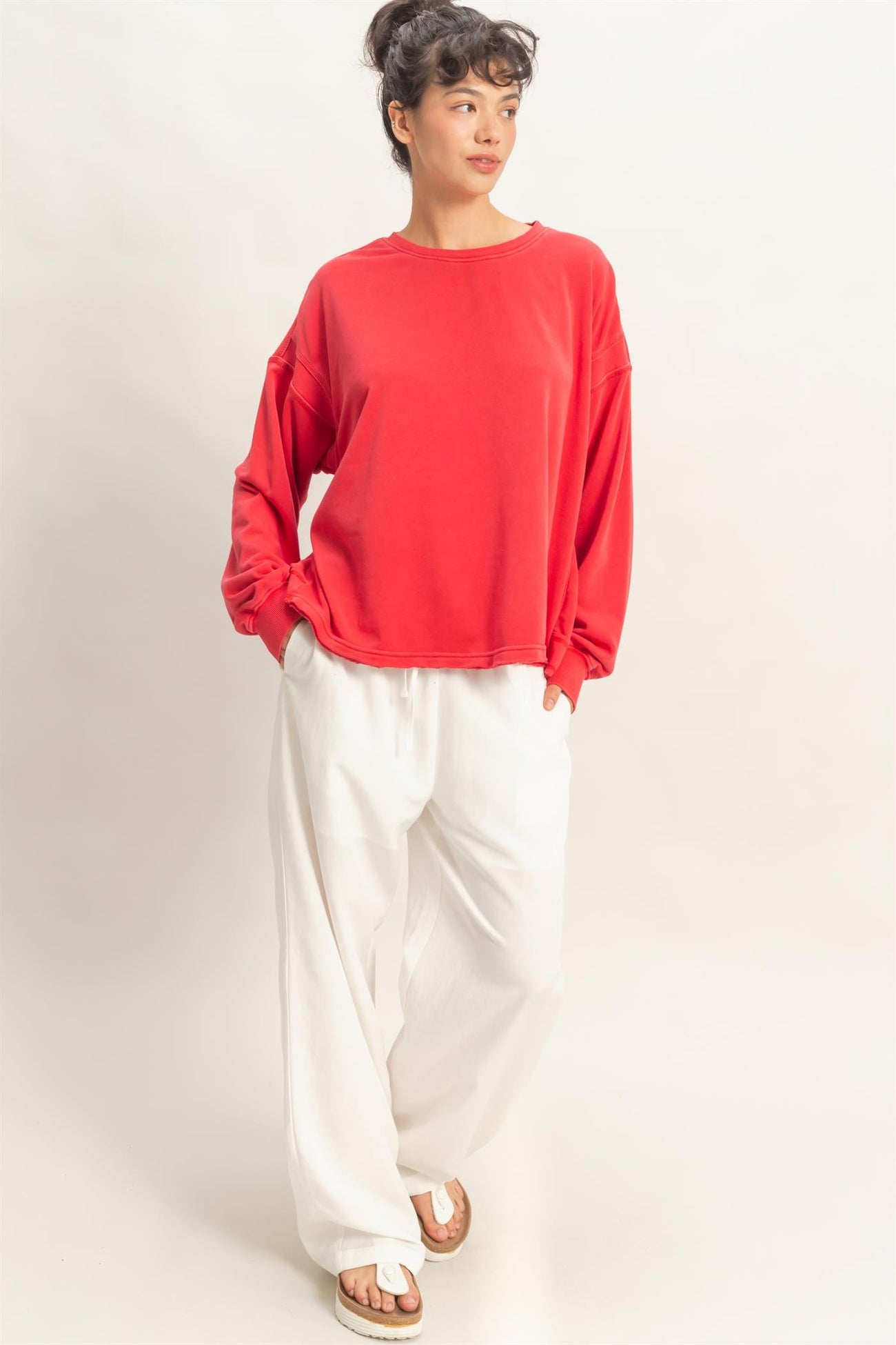 woman wearing a red oversized sweatshirt and white wide-leg pants, standing with hands in pockets