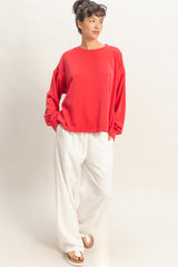 woman wearing a red oversized sweatshirt and white wide-leg pants, standing with hands in pockets