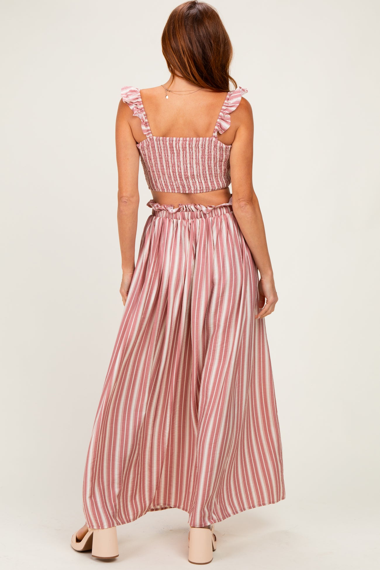 woman wearing a pink and white striped two-piece set with ruffled straps and a flowy maxi skirt