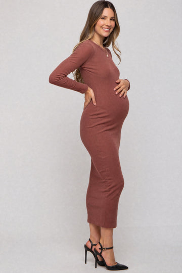 woman wearing a rust-colored long sleeve maternity dress and holding her baby bump