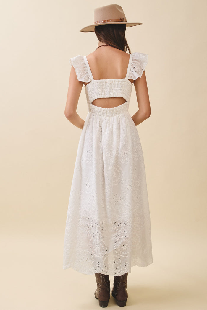 woman wearing a white maxi dress with ruffle sleeves and a cutout back, styled with a brown hat and cowboy boots
