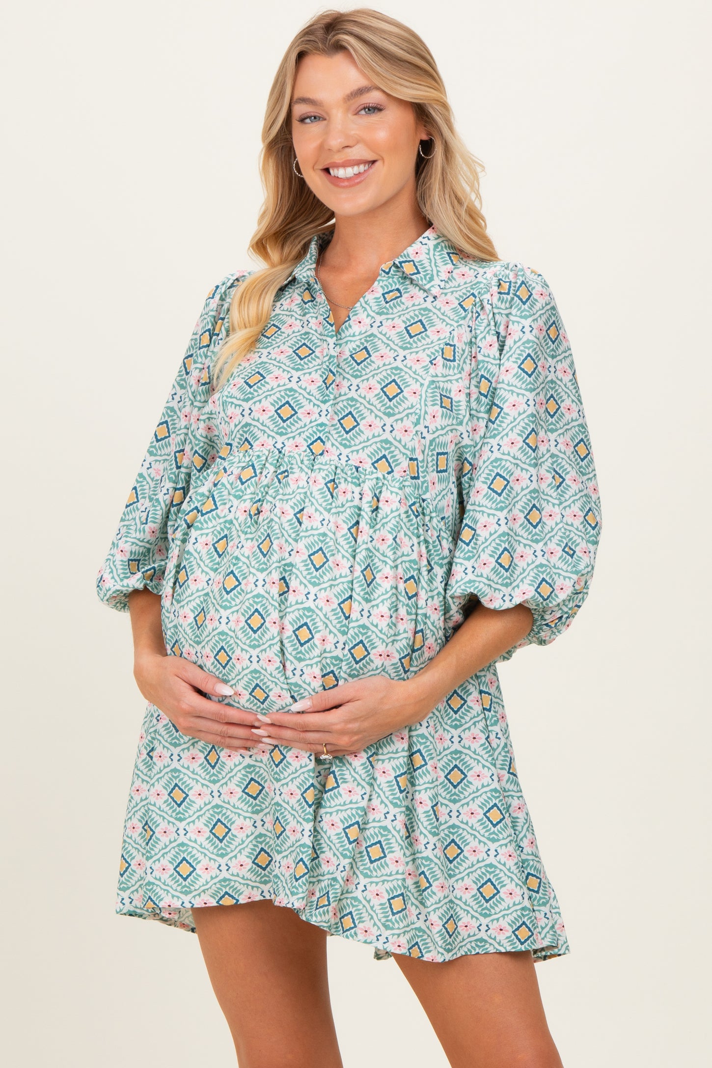 woman wearing a patterned green maternity dress with elbow-length sleeves and holding her baby bump