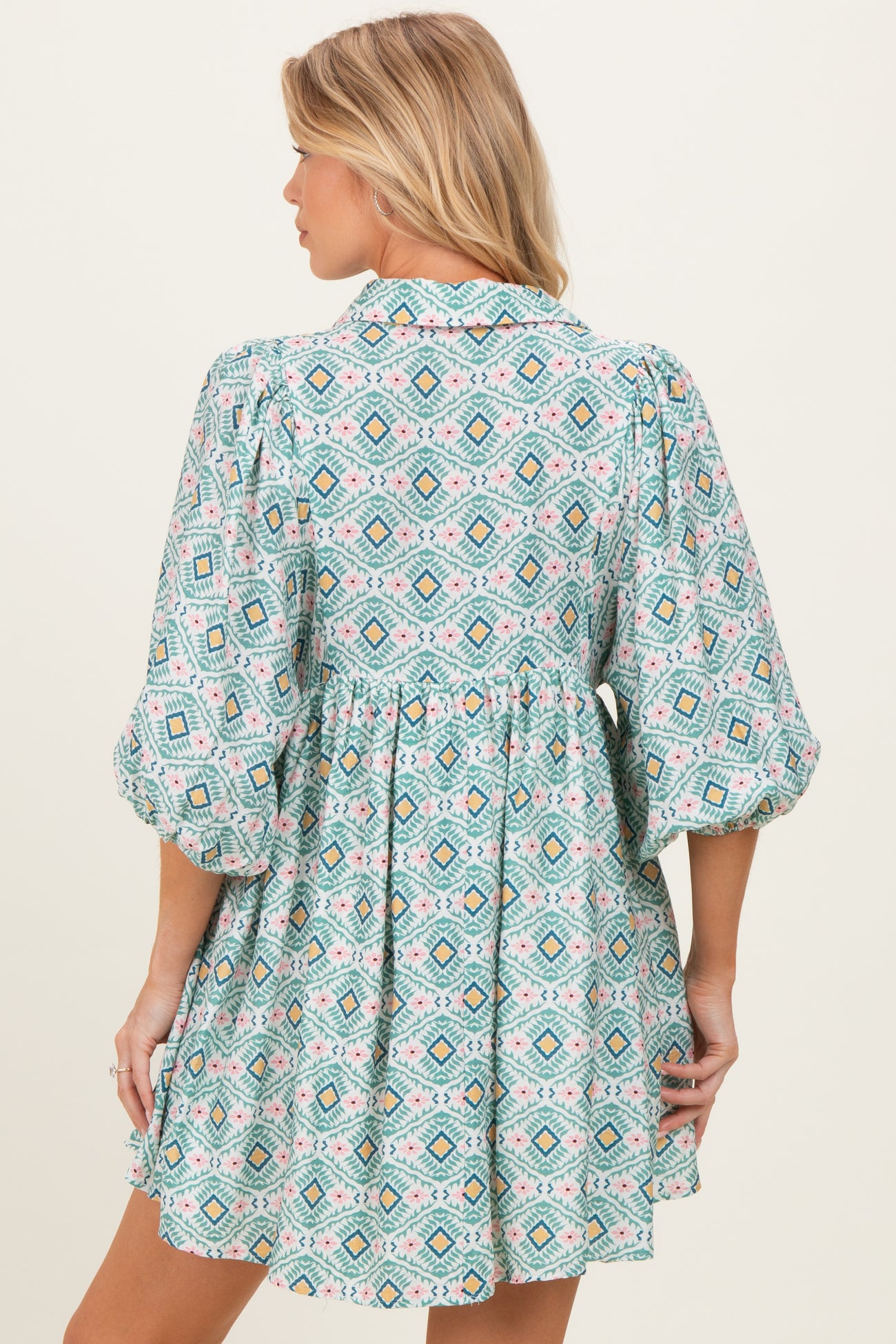 woman wearing a patterned turquoise maternity dress with puff sleeves and a loose fit, showing her baby bump from the back