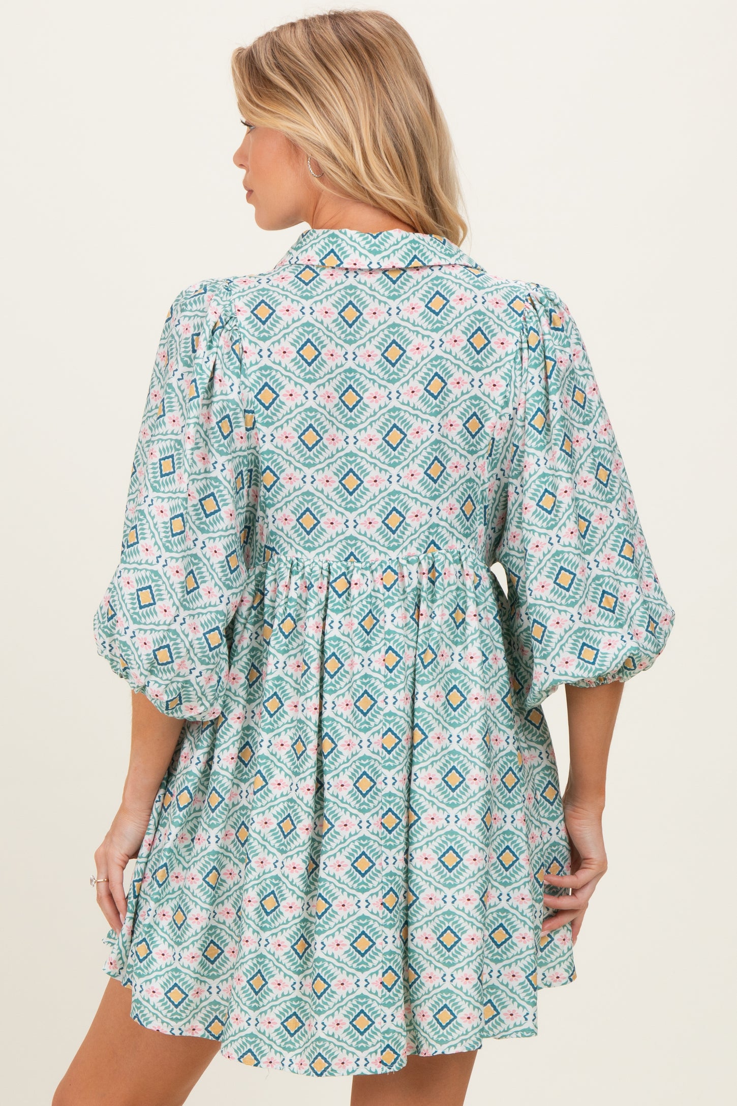 woman wearing a patterned turquoise maternity dress with puff sleeves and a loose fit, showing her baby bump from the back