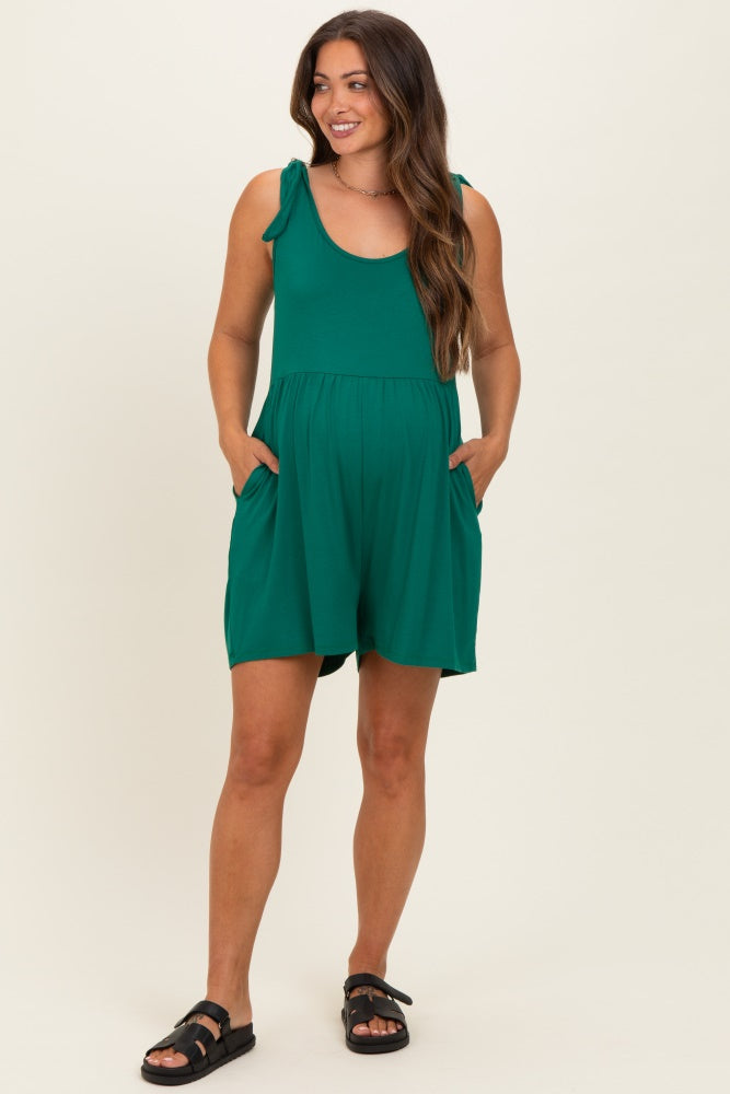woman wearing a green maternity romper with tie shoulder details and side pockets, showcasing her baby bump