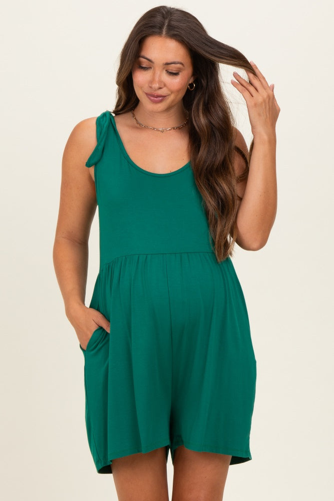 woman wearing a green maternity romper with adjustable shoulder ties and pockets, showing her baby bump