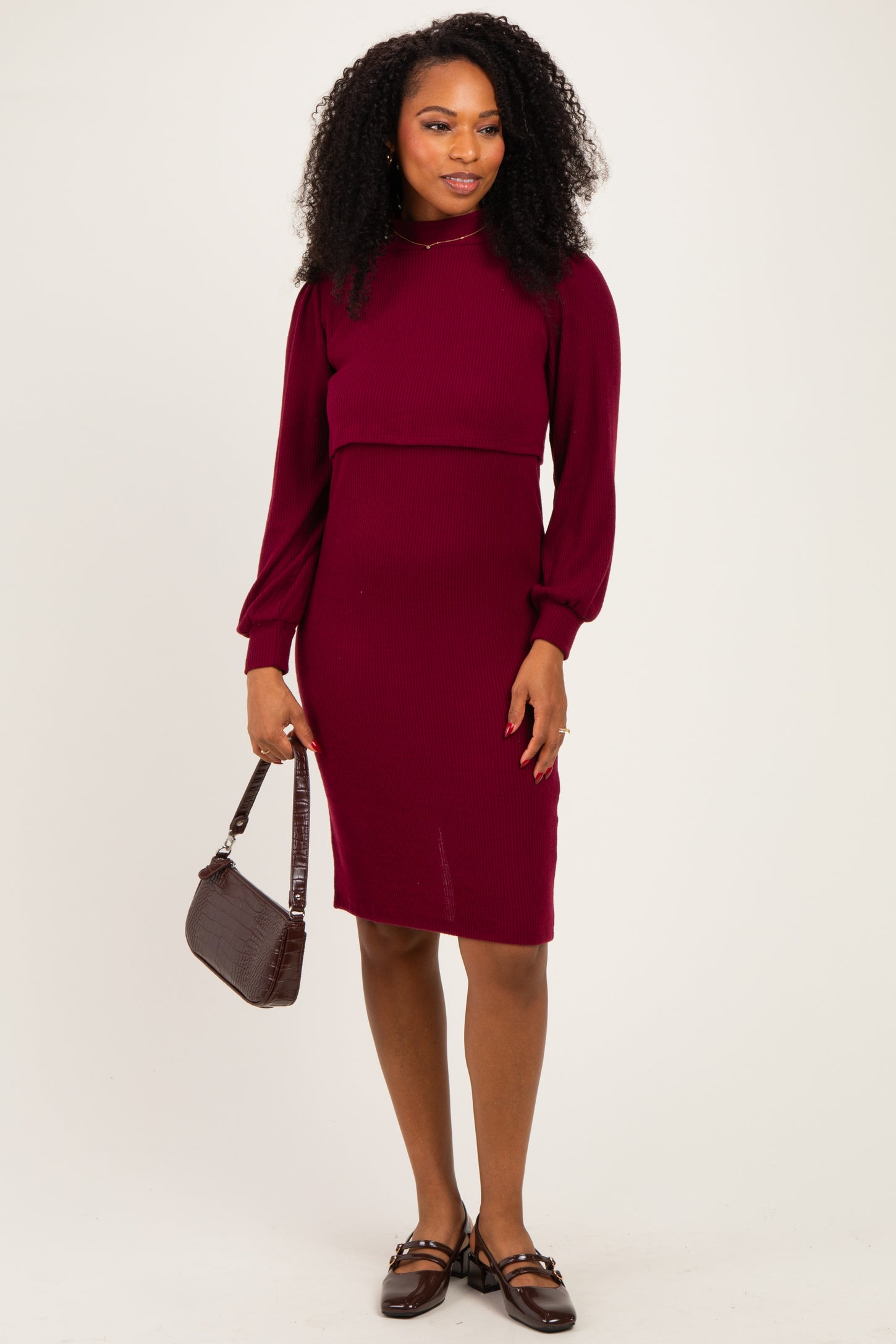 woman wearing a burgundy ribbed midi dress with long puff sleeves and a fitted skirt, holding a small brown handbag