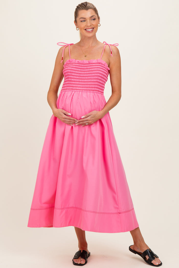woman wearing a bright pink maternity maxi dress with spaghetti straps and a gathered bodice, holding her baby bump