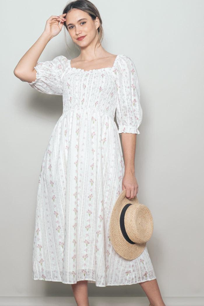 woman wearing a white floral midi dress with puffed sleeves and a square neckline, holding a straw hat