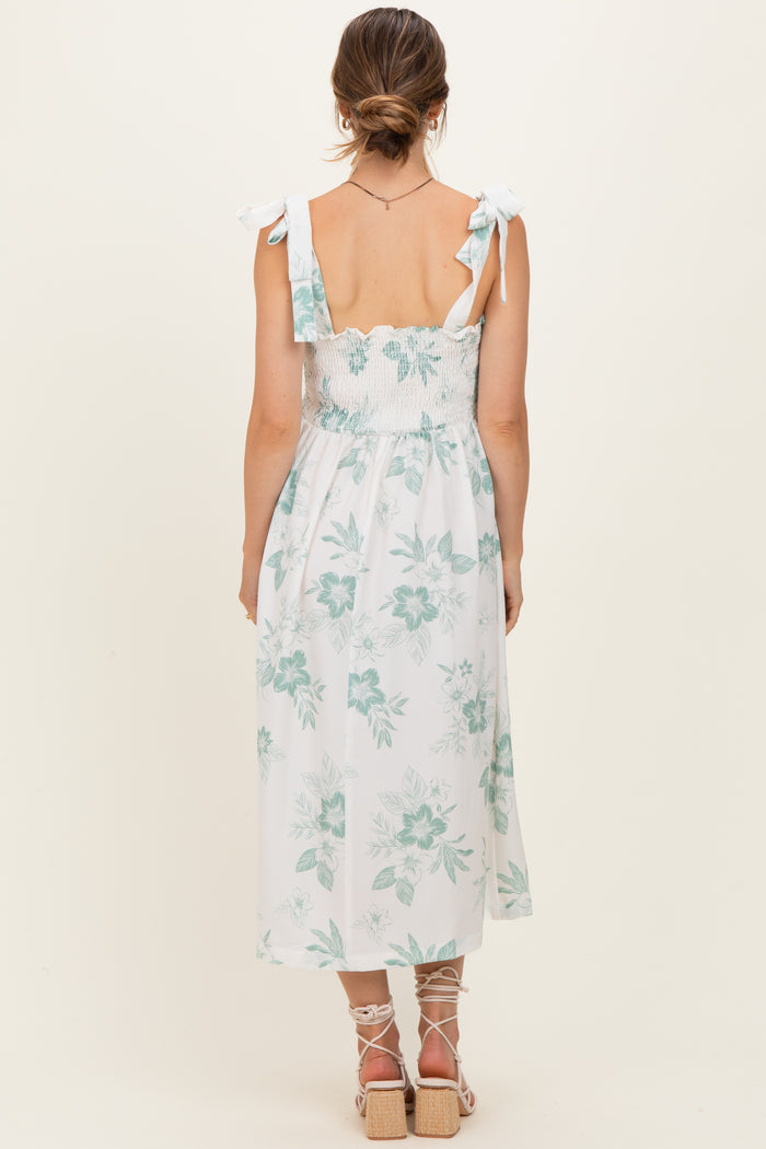 woman wearing a light blue and white floral maternity maxi dress with tie straps and a smocked bodice, showing a baby bump
